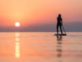 Back view of silhouette of unrecognizable female surfer standing on paddleboard and rowing against spectacular sun in su