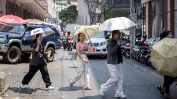 Hitzewelle in Thailand: Schwitzende Menschen auf einer Straße in Bangkok schützen sich mit Schirmen vor der Sonne.