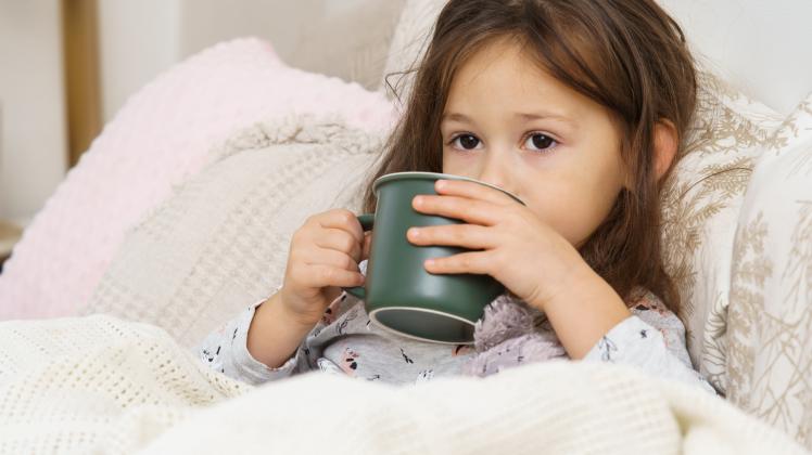 Nice, sweet, dear little dark haired preschooler girl drink hot tea or medicine from green mug, lying in pajamas in bed,