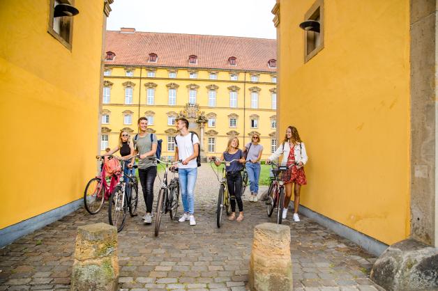Studierende treffen sich mit ihren Fahrrädern vor dem Erweiterungsbau und Schloss