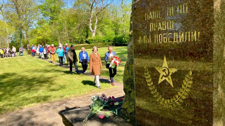 Menschen gehen mit Blumen auf ein sowjetisches Ehrenmal zu