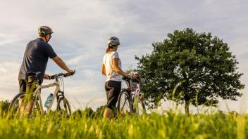 Couple is pushing their bikes over a meadow in the summer to find a place to rest from their long bike trip