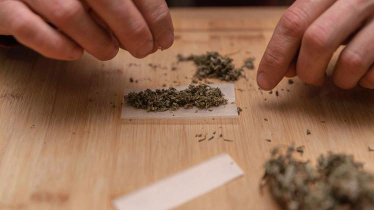 Anonymous male pinching dry cannabis buds while preparing for rolling blunt on wooden board, Model released RenataHamuda