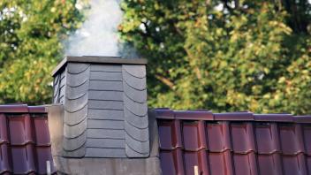 Energiekrise und Klimaschutz Rauchender Kamin eines Holzofens auf einen Dach während der kalten Jahreszeit um zusätzlich