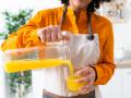 Young woman pouring orange juice in glass while standing at home model released Symbolfoto property released GIOF10052