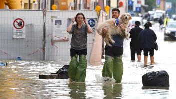 Pedestrians hold their dog in a flooded street in the town of Lugo on May 18, 2023, after heavy rains caused flooding across Italy&apos;s northern Emilia Romagna region. Rescue workers searched on May 18, 2023 for people still trapped by floodwaters in northeast Italy as more residents were evacuated after downpours which killed nine people and devastated homes and farms. (Photo by Andreas SOLARO / AFP)