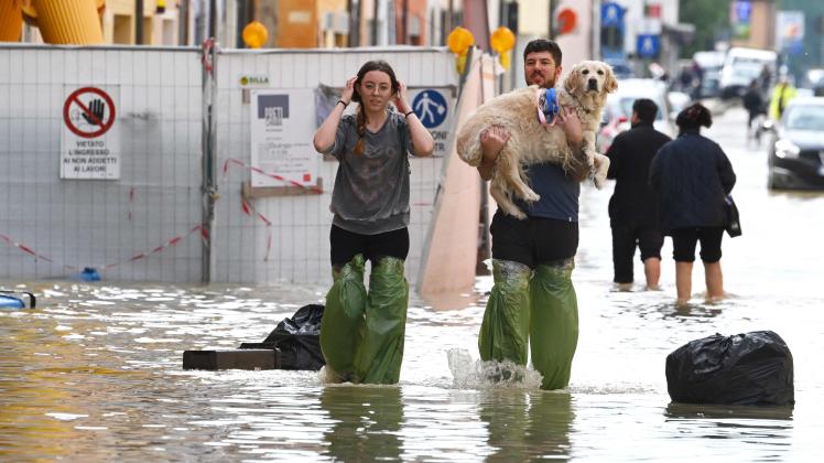 Pedestrians hold their dog in a flooded street in the town of Lugo on May 18, 2023, after heavy rains caused flooding across Italy's northern Emilia Romagna region. Rescue workers searched on May 18, 2023 for people still trapped by floodwaters in northeast Italy as more residents were evacuated after downpours which killed nine people and devastated homes and farms. (Photo by Andreas SOLARO / AFP)