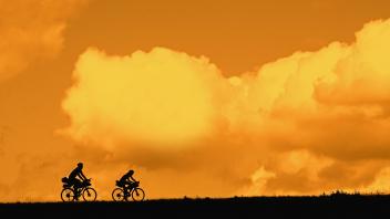 Couple of young cyclists riding their touring bicycles silhouetted against orange sunset sky in summer 3334BBFX