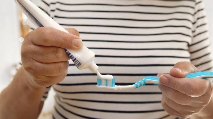 Frau traegt Zahnpasta auf eine Zahnbuerste auf woman applying toothpaste on a toothbrush BLWS681732 *** Woman carries To
