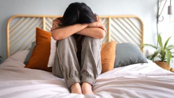Front view of depressed and sad young woman sitting on the bed crying. Sadness and mental health.