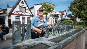 Tage der Kunst im öffentlichen Raum in Warnemünde: am Brunnen „Warnminner Ümgang” des Rostocker Bildhauers Wolfgang Friedrich spielte Klaus Lass groß auf.„Dick&apos;n Lass” gab neben auf Plattdütsch umgetexteten Klassikern wie „Heart of Gold” von Neil Young oder „Tequila Sunrise” von den Eagles auch viele Anekdoten aus dem Warnemünde seiner Kinderzeit zum besten. Die Bänke um den Brunnen waren gut besetzt - und der Craftbeer-Laden „Hoppen un Molt” gleich nebenan gut frequentiert... Foto: Georg Scharnweber