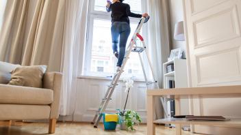 Frau auf Leiter putzt Fenster