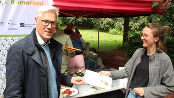 Glindes Bürgermeister Rainhard Zug erhält von Lisa Rück, wissenschaftliche Mitarbeiterin der Universität Flensburg, ein Rezept für einfache, klimafreundliche Gemüsepuffer.
