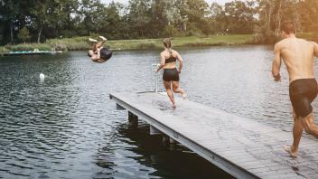 Sportive people running on jetty jumping into lake after workout training model released Symbolfoto