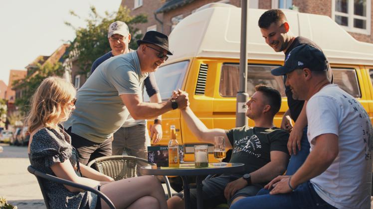 Eine Szene aus dem Musikvideo: Die Mitglieder von „Black Dog Thula“ treffen vor der Kneipe „Malör“ im Ortskern von Emsbüren auf das junge Paar, das im Video das Emsland für sich entdeckt. 