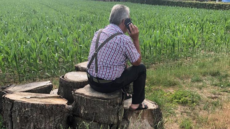 Günter Diersing sitzt zum Telefonieren auf dem freien Feld auf einem Holzstapel.