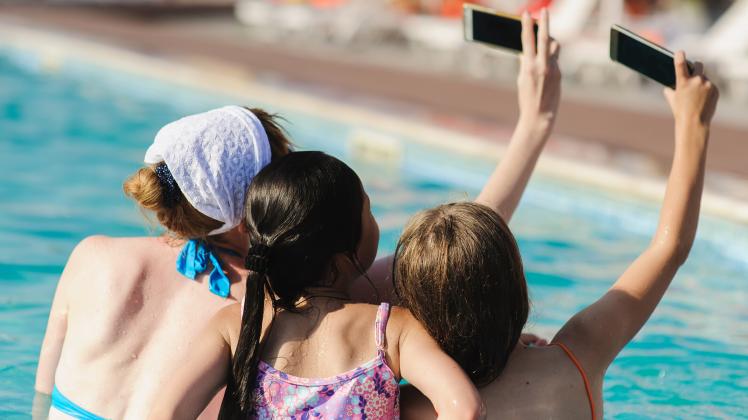 Tree beautiful girl photographed themselves on the phone in swimming pool. Woman and two teenage girls make selfie. View from the back. (OLypa)