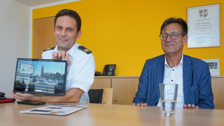 Dr. Stephan Jakobi (l.), Leiter des Fachdienstes Feuerwehr und Katastrophenschutz, und Baudezernent Bernd Nottebaum zeigen anhand eines Beispiels aus Hamburg, wie die Warnungen auf den digitalen Werbetafeln aussehen können.