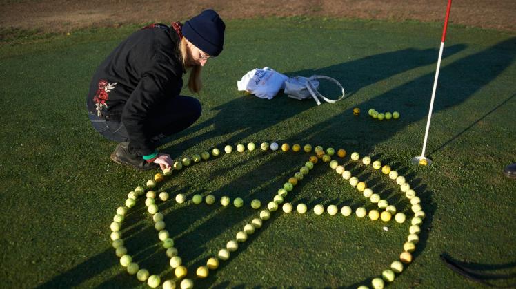 XR Activists Block A Golf Course A young woman draws the XR symbol on the golf course with golf balls found on the golf.