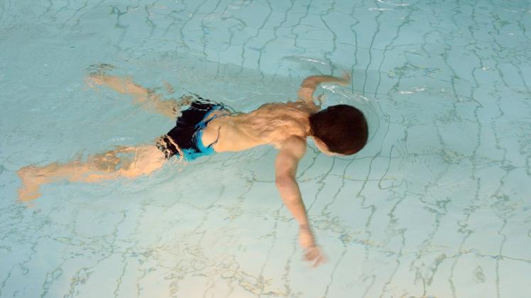 Ein kleiner Junge schwimmt mit untergetauchtem Kopf an der Wasseroberfläche eines Schwimmbeckens.