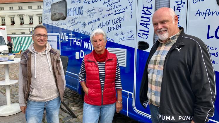 Zwei Männer und eine Frau vor einem Wohnmobil von der Organisation „Blaues Kreuz“.