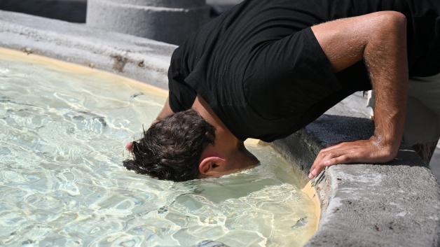 TOPSHOT - A man puts his head in the water to cool off at the fountain in Piazza del Popolo in Rome, on July 18, 2023. Europe braced for new high temperatures on July 18, 2023, under a relentless heatwave and wildfires that have scorched swathes of the Northern Hemisphere, forcing the evacuation of 1,200 children close to a Greek seaside resort. (Photo by Tiziana FABI / AFP)