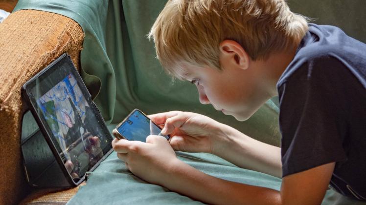 Russia, Moscow. A boy is playing a mobile game on his phone, lying on the couch. KonstaninxKokoshkin