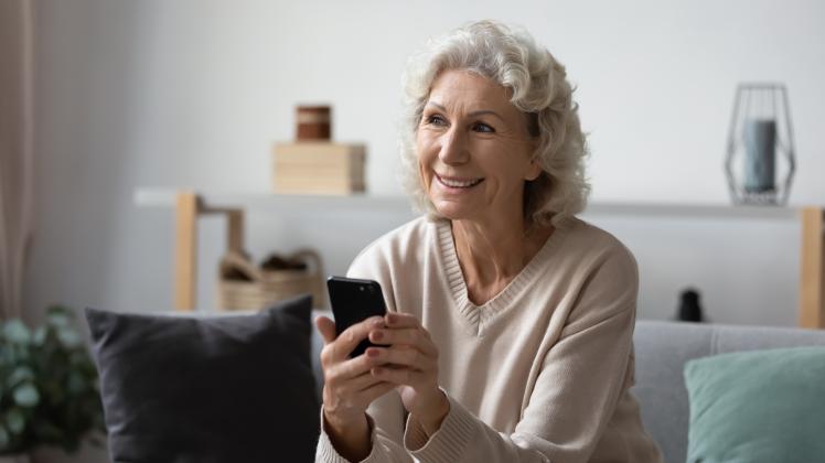 Dreamy  happy  hoary  mature  elderly  woman  holding  smartphone,  feeling  positive  about  receiv
