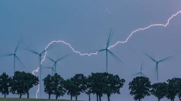 Ein Blitz erhellt den Abendhimmel Ã¼ber der Landschaft mit Windenergieanlagen im Landkreis Oder-Spree. 
