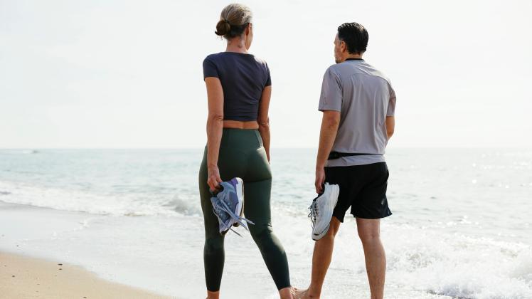Couple holding sports shoes walking near shore at beach model released, Symbolfoto, EBSF03268