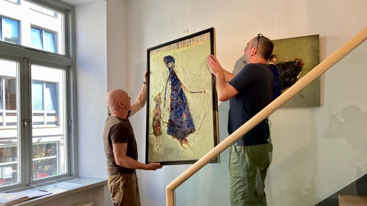 Zwei Männer hängen das Werk eines Malers in einer Galerie auf.