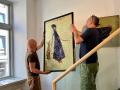 Zwei Männer hängen das Werk eines Malers in einer Galerie auf.