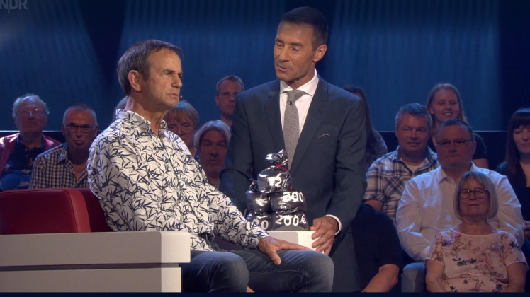 Der Meppener Peter Höfer (links) an der Seite von Moderator Kai Pflaume. Auf der Armlehne zu sehen sind die „Geldsäcke“, die zeigen, dass Peter Höfer 1000 Euro gewonnen hat.