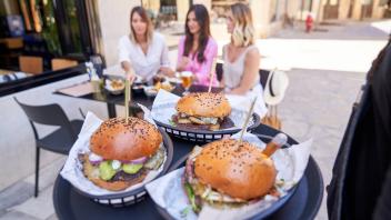Faceless man carrying tray with burgers while serving trendy women at table in sidewalk cafe Copyright: xPhilippexDegroo