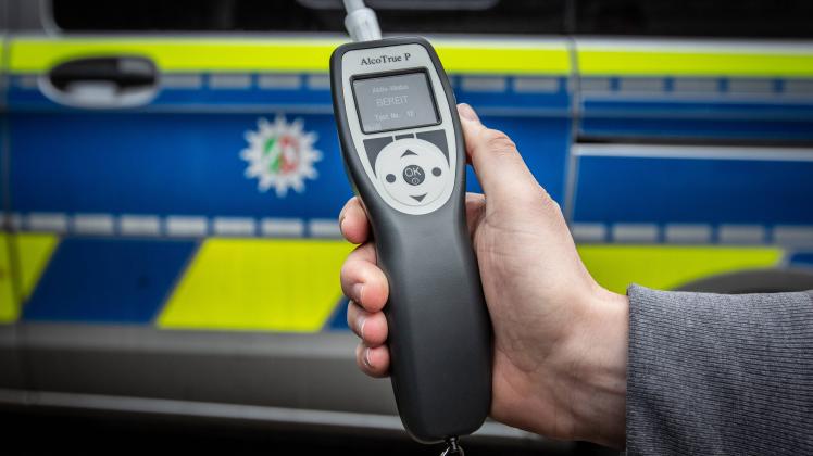 Symbolbild Thema Polizei, Hand mit Alkoholtester, Testgeraet vor einem Einsatzwagen Symbolbild zum Thema Polizei am 22.0
