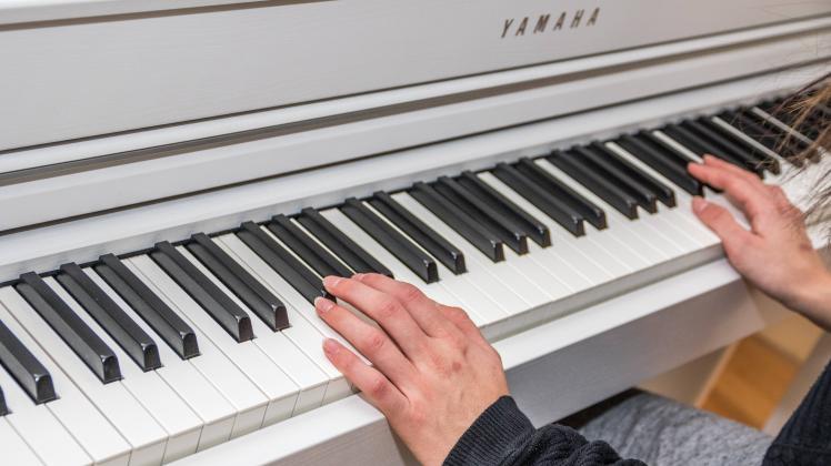 Nahaufnahme Hände auf Klaviatur Langhaarige junge Frau spielt zuhause auf weißem Digitalpiano von Y
