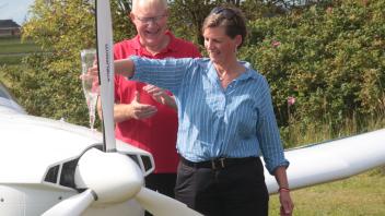 Bis zum letzten Tropfen: Mit Wasser aus der Lecker Au tauft Bianca Meyerhoff das Ultraleichtflugzeug auf den Namen Hinrich Frerichs – zur Erinnerung an den 2021 verstorbenen Stifter. Harald Clasen applaudiert.