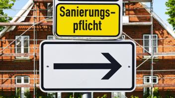 FOTOMONTAGE, Schild mit Pfeil und Aufschrift Sanierungspflicht vor eingerüstetem Haus *** PHOTOMONTAGE, sign with arrow 