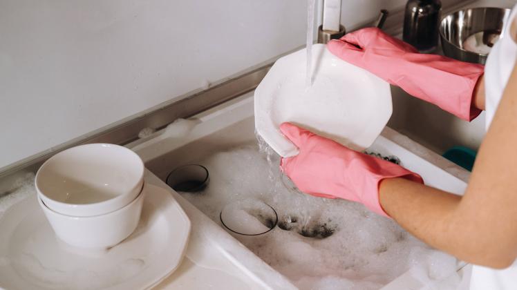 RECORD DATE NOT STATED housewife girl in pink gloves washes dishes by hand in the sink with detergent. The girl cleans t