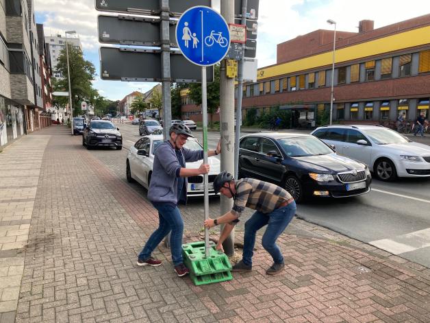 Gerd Gramberg (links) und Moritz Niemann vom Fachdienst Verkehr beseitigen das erste Problem: Das Fußgänger- und Radfahrerschild gegenüber der Post stand mitten auf dem und damit im Weg, obwohl es auch am Rand gut zu erkennen ist.