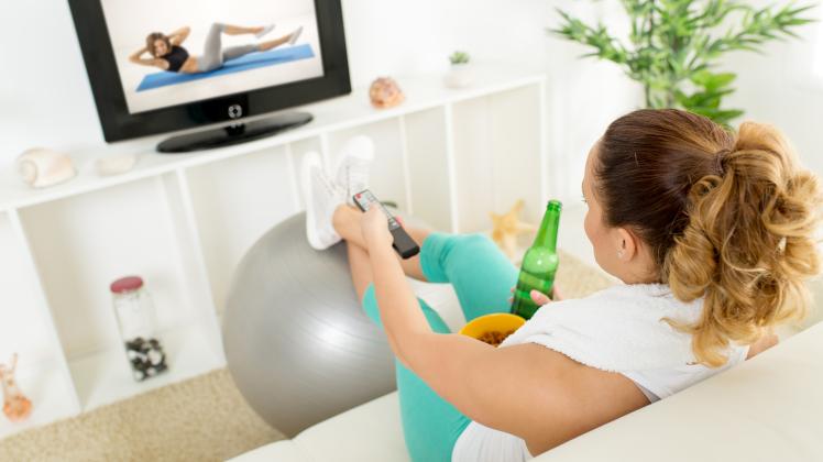 Lazy  woman  in  sport  clothing  sitting  front  of  the  TV  and  doesn't  wont  to  exercise. Mod