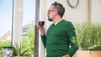 Ein Mann steht mit einer Tassee Kaffee am Fenster.