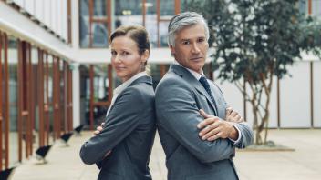 Mature business man and woman standing back to back looking at camera model released Symbolfoto prop