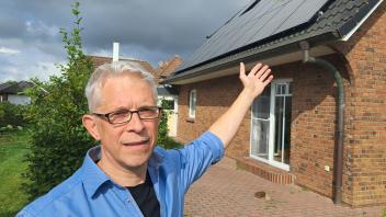 Der Niebüller SPD-Fraktionschef Andreas Esch steht am 22.9.2023 in seinem Garten und zeigt auf PV-Anlagen auf seinem Hausdach.