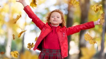 Beautiful red-haired girl in the autumn park scatters maple leaves. Beautiful red-haired girl in the autumn park scatter