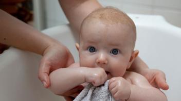 Person hält Baby in Badewanne