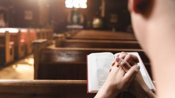 Olden, Norway - July 13, 2023: Young man praying to God in church with a Bible and folded hands. Faith in religion and f