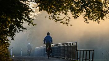 Radfahrer fahren im Nebel über eine Brücke.
