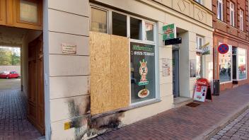 Die Schäden an dem Haus in der Gleviner Straße sind noch deutlich zu sehen. Die Scheibe der Pizzeria wurde vorerst durch eine Pressspanplatte ersetzt.