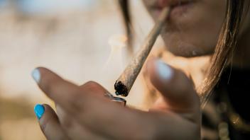 Young woman igniting marijuana cigarette outdoors model released Symbolfoto ACPF01230
